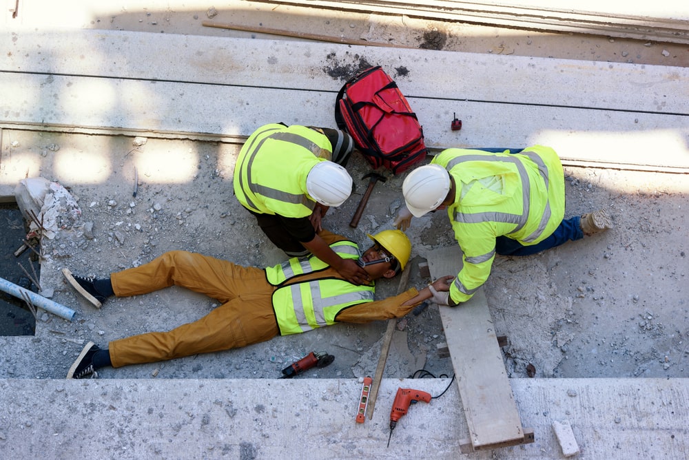 Construction Worker Laying On The Ground Being Checked Upon By His Colleagues